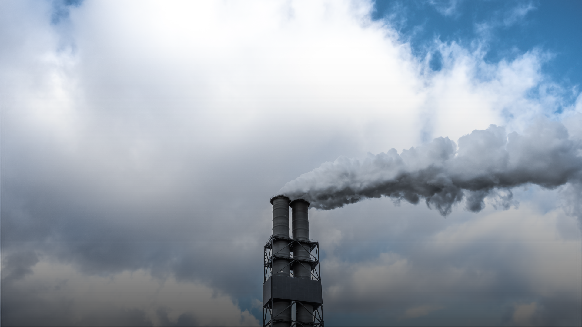 Chimney with smoke blowing out against the backdrop of a sky.